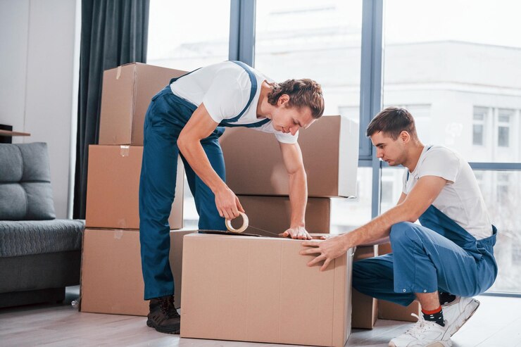 packaging-box-two-young-movers-blue-uniform-working-indoors-room_146671-52043